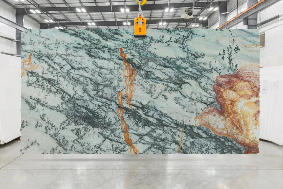 Large quartzite slab panel with a pale blue-green base and prominent dark gray veining plus warm orange-gold veining, photographed hanging in a warehouse or showroom.
