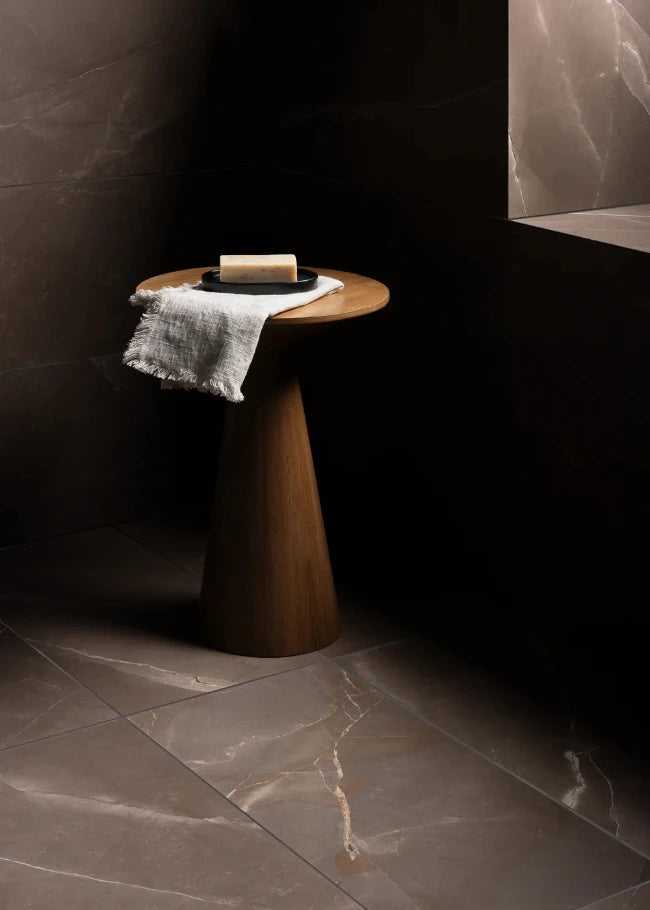Wooden side table with a white towel and bar of soap and a dark brown marble tile floor