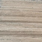 A close-up texture of a travertine stone slab surface with horizontal striations in warm beige, taupe, and light brown tones.