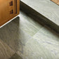 Close-up of a green tiled floor with a wooden cabinet and doormat in the background
