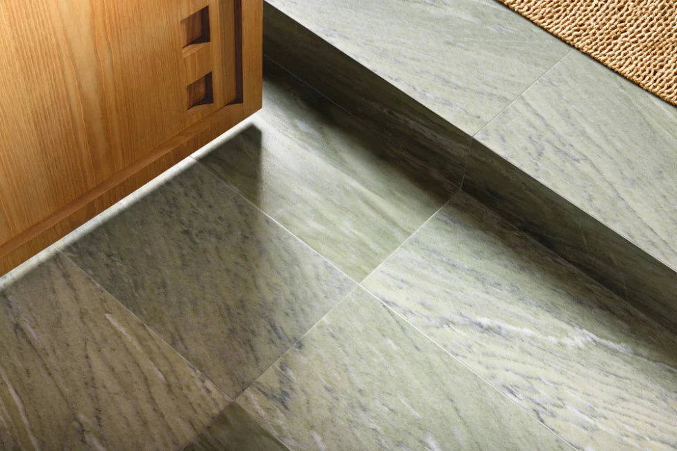 Close-up of a green tiled floor with a wooden cabinet and doormat in the background